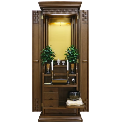 Open wooden home Buddhist altar cabinet (butsudan) with plants, candles, and offerings inside a small shrine.