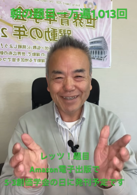 Smiling man in a light jacket speaks to camera in an office; green Japanese text overlays advertise a talk about Amazon e-publishing behind him