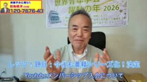 Smiling Japanese man in a light jacket sits at a desk, hands raised mid-gesture, with a banner behind and a yellow ad in the top-left corner, discussing YouTube memberships in Japanese text auf.