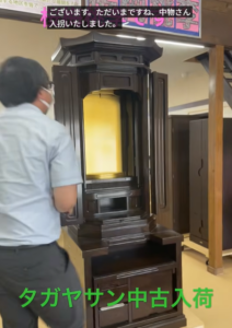 Man wearing a mask stands beside a tall, ornate dark wooden Buddhist altar with its doors open, revealing the gold inner shrine.