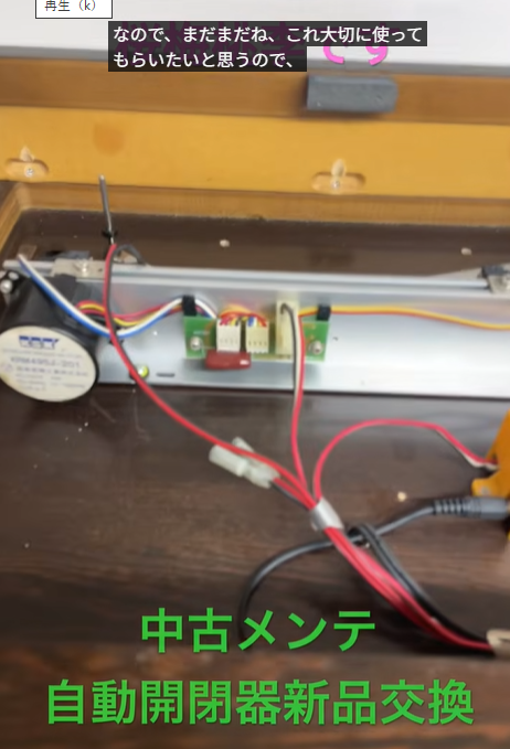 木製の箱の中にある自動開閉機の回路基板と赤黒の配線。機械の内部構造を示す写真。