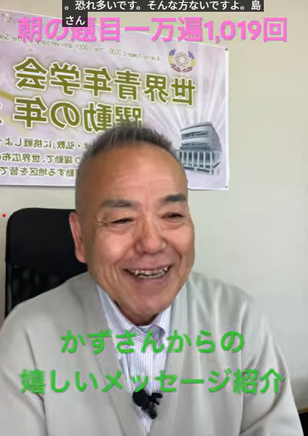 Smiling Japanese man in a light suit sits in an office, banner behind him with Japanese text and colorful captions overlaid.