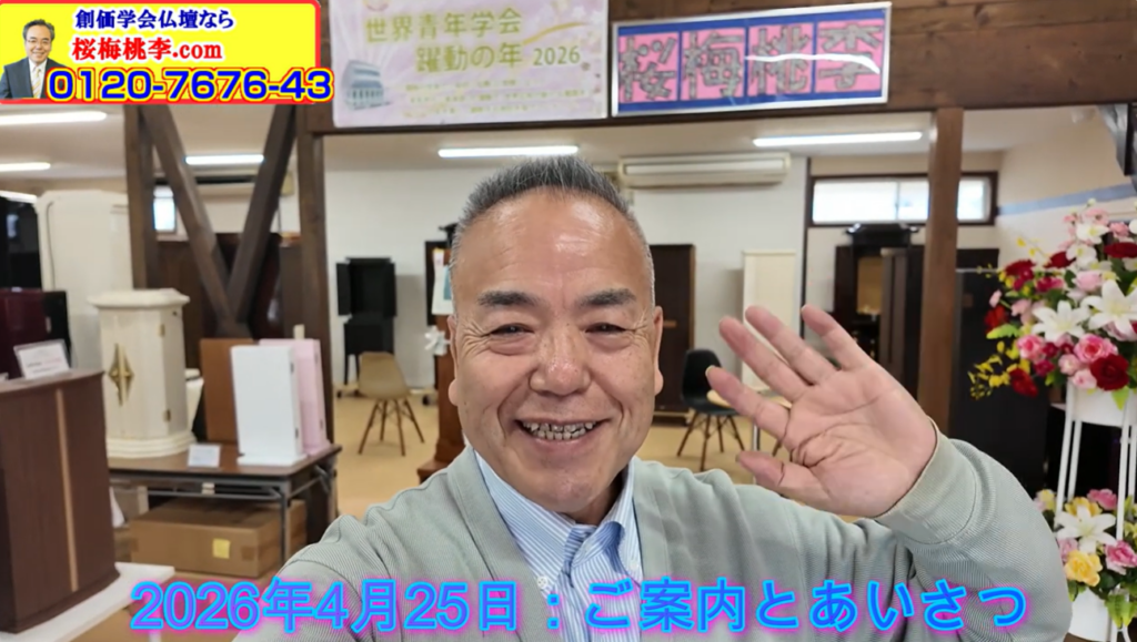 Smiling man waves at the camera in a shop, with banners and flowers in the background; blue text overlay reads '2026年4月25日：ご案内とあいさつ'.