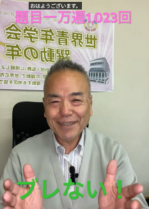 Smiling older man in a light cardigan, giving a thumbs-up, with a banner behind him; overlaid Japanese text includes 'おはようございます' and 'ブレない！'