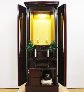 Open dark wooden altar cabinet with a gold interior, featuring candles, small floral ornaments, and potted plants on tiered shelves.