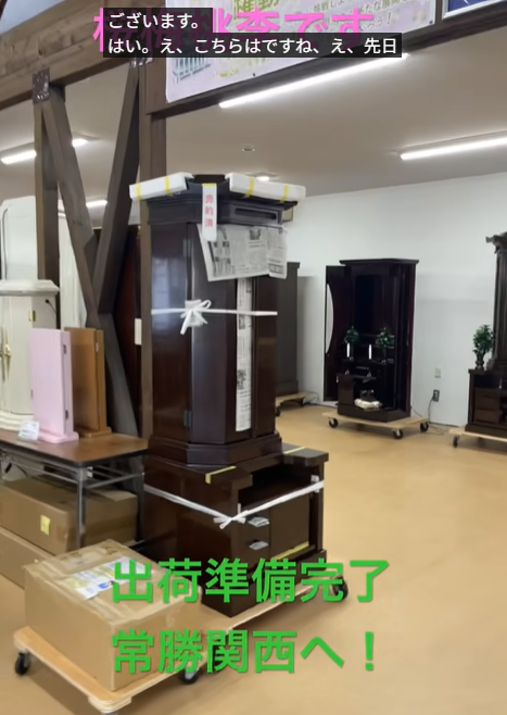 Tall dark wooden Buddhist altars on wheeled carts, strapped for transport in a warehouse-like space with boxes around.