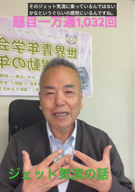 Middle-aged man in a jacket speaks to camera, hands clasped, with a banner behind him and the green caption 'ジェット気流の話'.