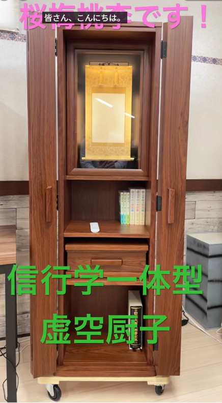 Wooden butsudan on wheels with an inner gold shrine, open doors, and a few books on a shelf; pink banner text at top and green banner text across the front in Japanese.