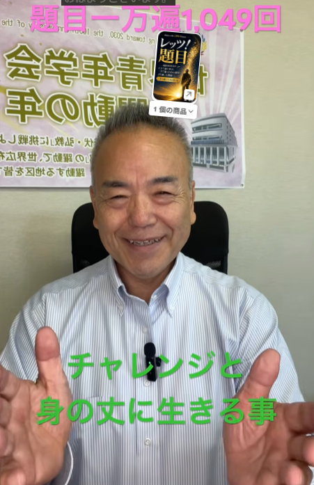 Smiling man in a light striped shirt sits and shows two thumbs up; green Japanese text overlay reads 'チャレンジと身の丈に生きる事' with a poster in the background.