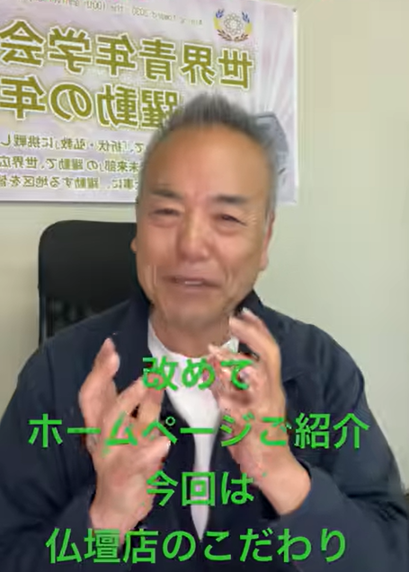 Older man in an office, speaking and gesturing with his hands. A poster with large Japanese text is on the wall behind him; green overlay text reads: '改めて ホームページご紹介 今回は 仏壇店のこだわり'.