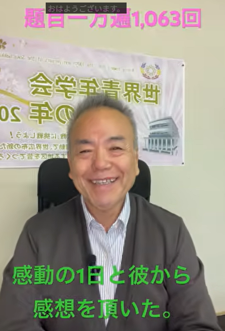 Smiling man in a suit seated in an office with a banner behind him; green Japanese subtitles read: 感動の1日と彼から感想を頂いた。 Likely a video or livestream.