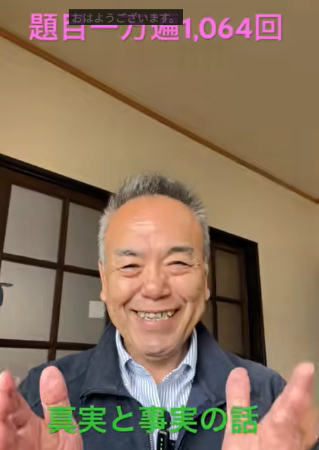 Smiling older man in a jacket gestures with both hands while speaking in a room; on-screen Japanese captions read '真実と事実の話' with a pink banner showing a count (1,064回).