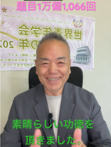 Smiling man in a gray suit sits in an office, giving a thumbs-up with a green caption in Japanese that reads '素晴らしい功徳を頂きました'.