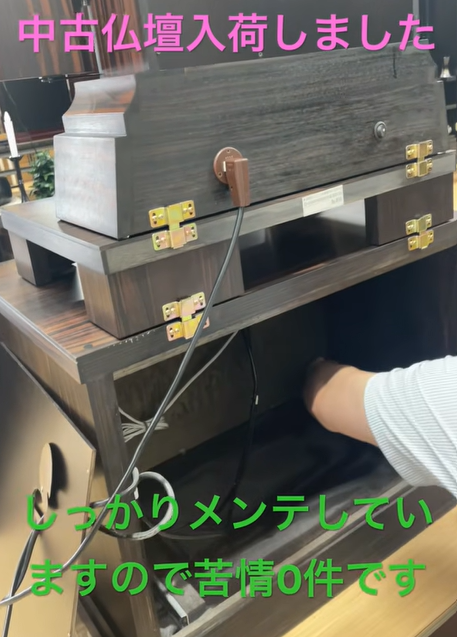 Used Buddhist altar just arrived and being carefully maintained; a person is visible nearby with the cord plugged in. Overlay text in pink/green Japanese announces arrival and maintenance.