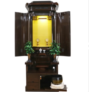 Traditional Japanese butsudan household altar with a gilded inner shrine, open doors, and two small plants on the sides.
