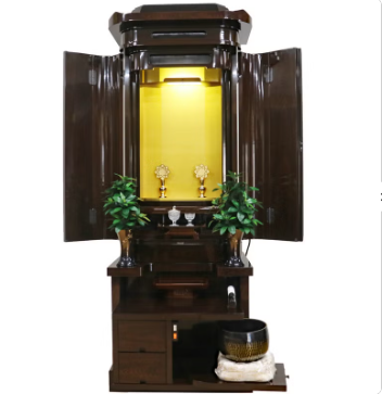 Traditional Japanese butsudan household altar with a gilded inner shrine, open doors, and two small plants on the sides.