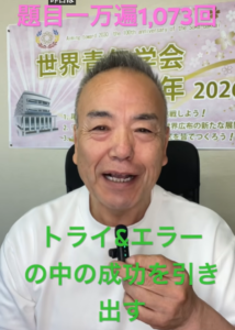 Smiling man in a white shirt speaks to the camera, with a colorful banner behind him and bold green Japanese text overlay.