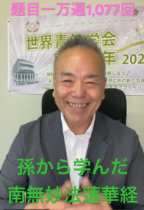 Smiling man in a suit seated in front of a banner with Japanese text, pink title at the top and green caption at the bottom.
