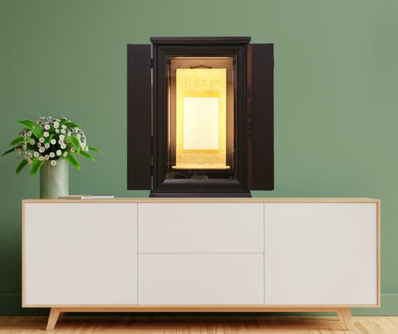 Modern sideboard against a green wall with a dark open cabinet housing a glowing gold shrine; a vase of white flowers sits on the left.