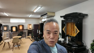 Man taking a selfie in a showroom with chairs and display cases in the background, and a large black ornate cabinet with gold interior nearby.