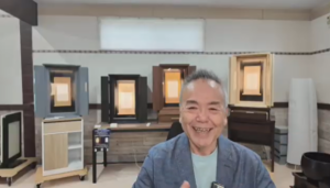Smiling man in a frame shop showroom with wooden picture frames displayed on shelves behind him.