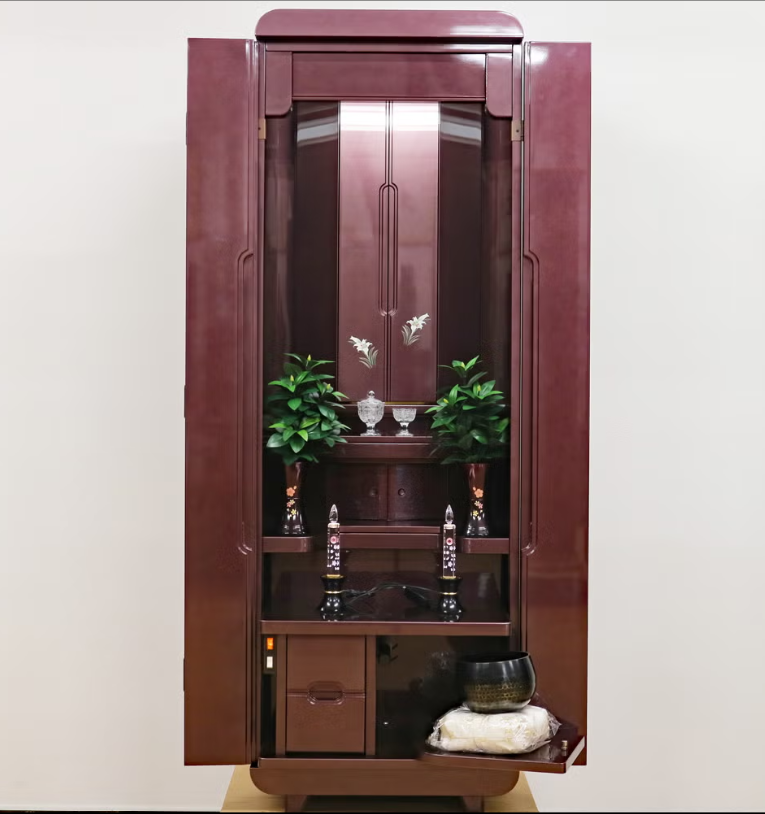 Tall mahogany home altar with open doors, central decorative panel, and ceremonial items on shelves against a light wall.
