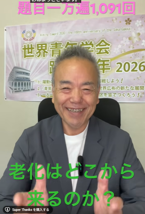 Smiling man in a suit speaks to the camera, with an informational banner about aging in the background and a green caption asking, 'Where does aging come from?'