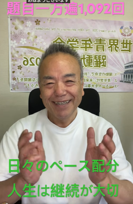 Smiling man in a white shirt sits before a banner, hands raised as if clapping; pink headline at top and green Japanese captions at bottom.