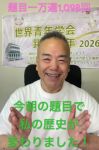 Smiling man sitting indoors with a banner in the background; green Japanese text across his chest says the topic changed his history, pink text above.