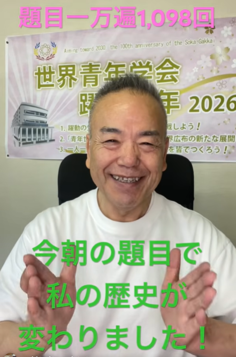 Smiling man sitting indoors with a banner in the background; green Japanese text across his chest says the topic changed his history, pink text above.