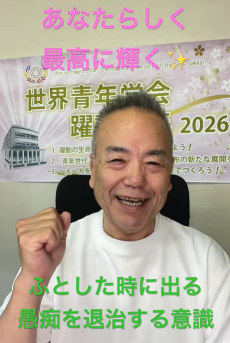 Smiling man raising a fist in front of a banner with Japanese text promoting positivity and self-improvement, emitting a cheerful, motivational vibe.