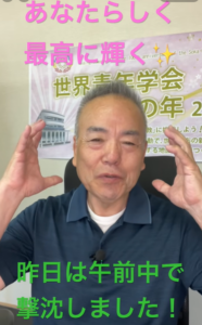 Middle-aged man in a blue polo speaks to the camera with hands raised; background banner and colorful Japanese captions at top and bottom.