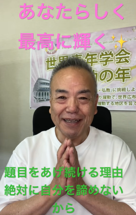 Smiling Japanese man in a white shirt sits indoors with hands pressed together in a prayer-like gesture; bright pink Japanese text overlays say “あなたらしく 最高に輝く” and green text below conveys a motivational message.