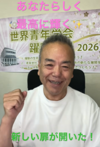 Smiling man in a white shirt with his fist raised, seated in front of a colorful banner advertising a 2026 event.