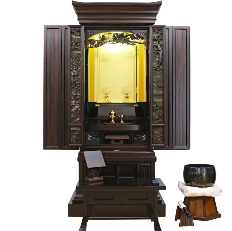 Dark wooden Buddhist altar (butsudan) with doors open, revealing a golden inner shrine and small offerings; a prayer desk sits in front with a bowl on a stand nearby.
