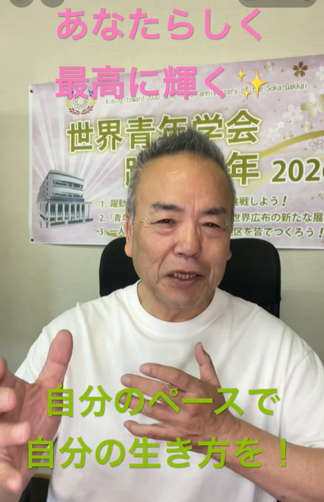 Smiling man in a white shirt speaks to the camera, with a poster behind him and pink text at the top reading 'あなたらしく 最高に輝く' and green text at the bottom reading '自分のペースで 自分の生き方を！'