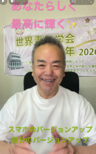 Smiling man on a video call with a Japanese event poster behind him; green caption at bottom reads 'スマホのバージョンアップ 自分のバージョンアップ'.