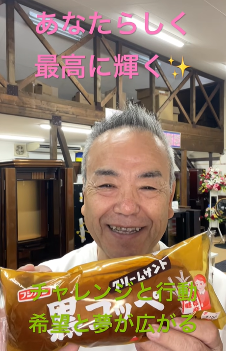 Smiling man in a store holding a brown snack bag toward the camera with pink and green motivational captions overlaid in Japanese.