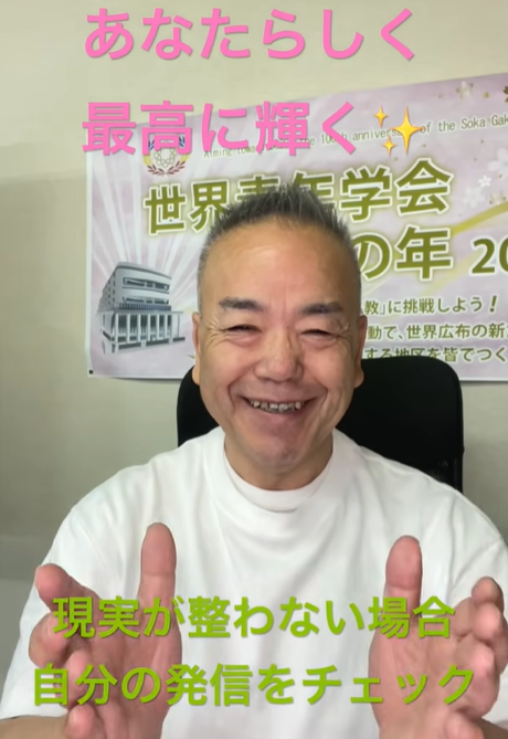 Smiling man in a white shirt facing the camera, hands raised, with a banner behind him and pink text above: 'あなたらしく 最高に輝く' and green text below: '現実が整わない場合 自分の発信をチェック'.