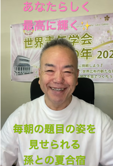 Smiling man in a white shirt sits in front of a banner with pink Japanese caption across the top reading 'あなたらしく最高に輝く' and green text across the bottom saying '毎朝の題目の姿を見せられる 孫との夏合宿'.