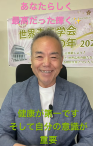Smiling man in a blue blazer in front of a poster; pink text at top and green text at bottom convey messages about being yourself and health first.